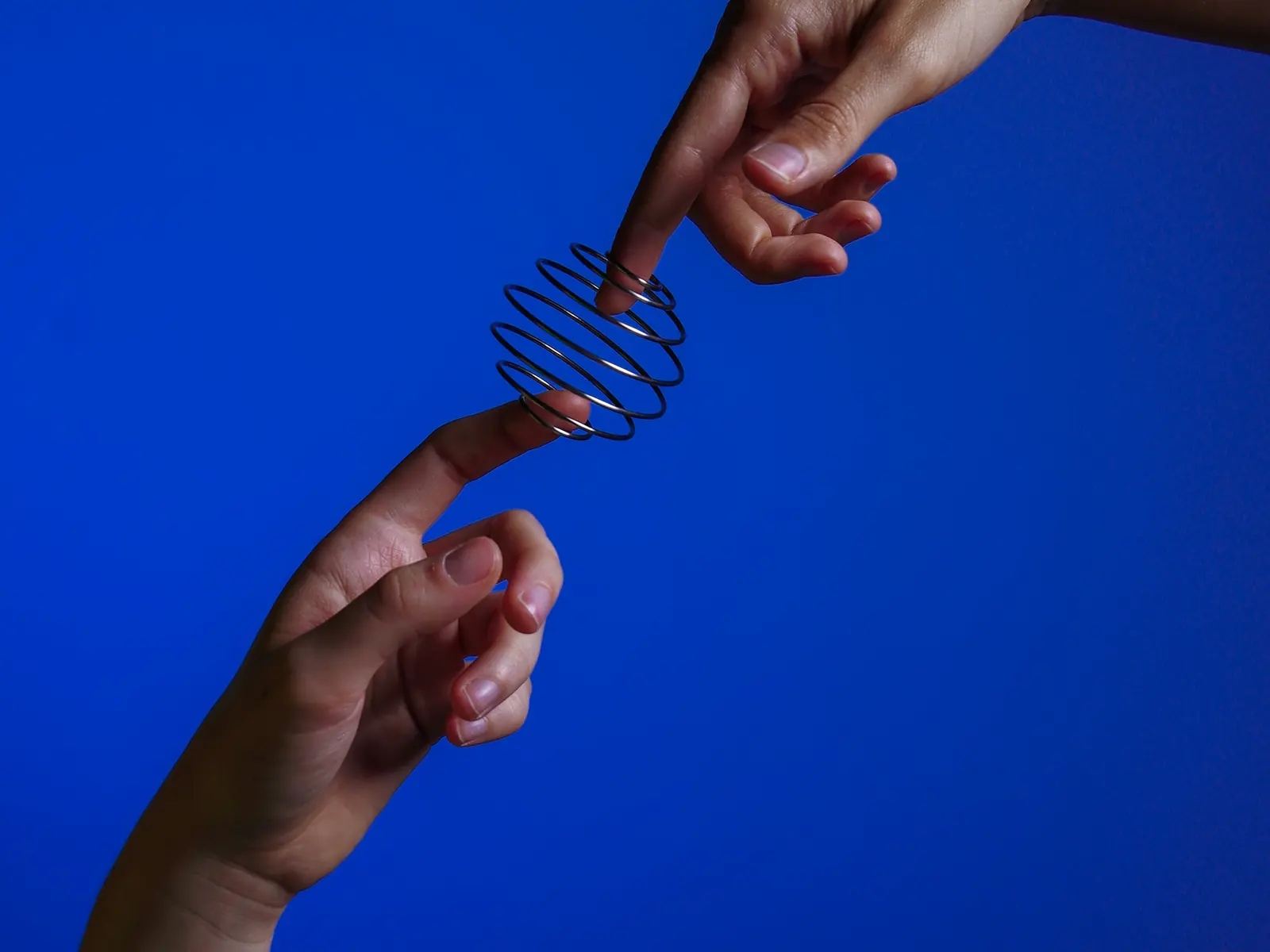 Two hands passing a metal spiral against a deep blue background
