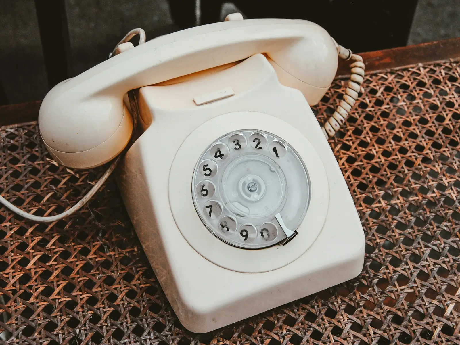 Téléphone à cadran couleur crème posé sur une assise en cannage