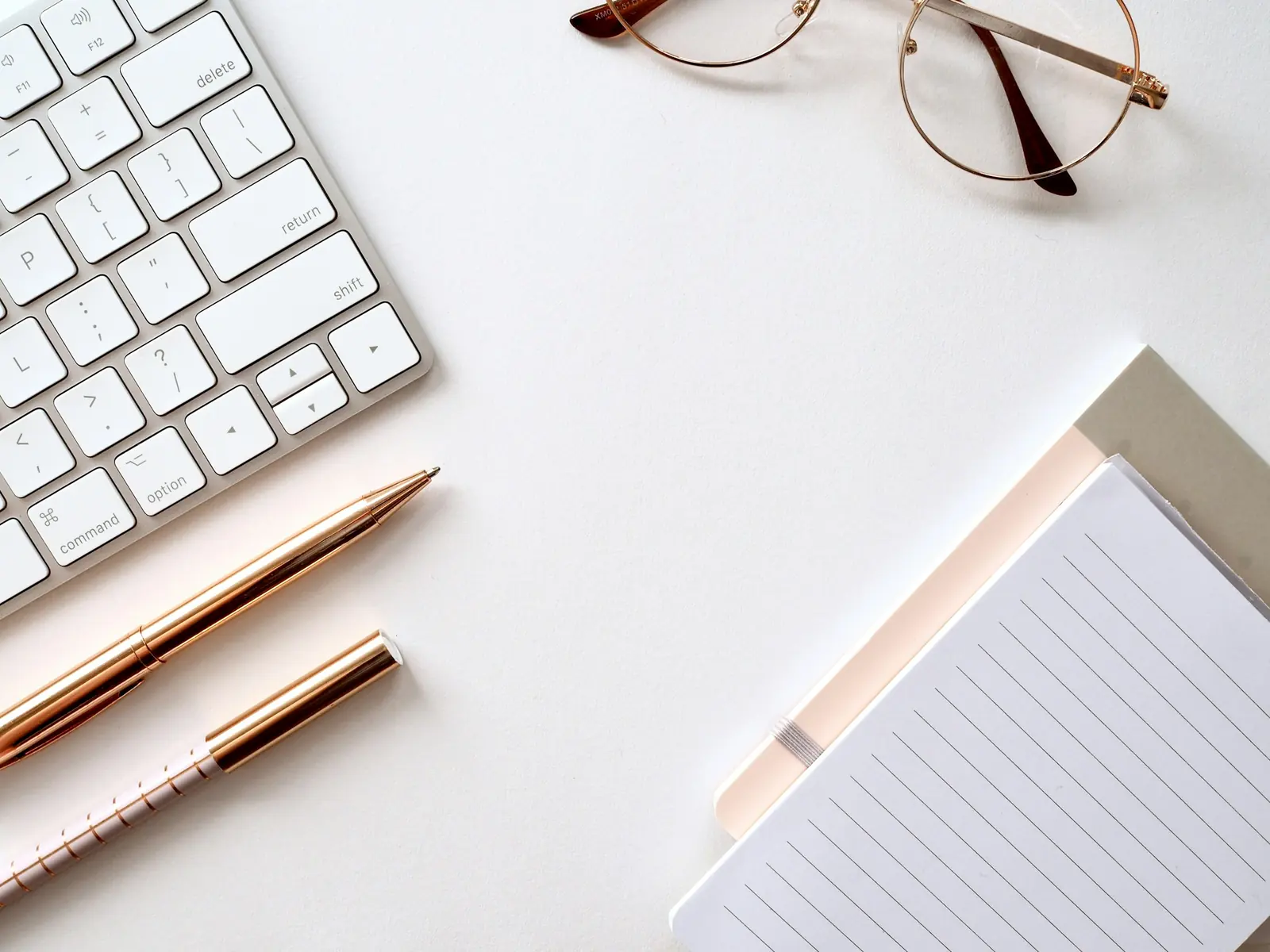 Keyboard, notebook, pens and glasses on a white desk
